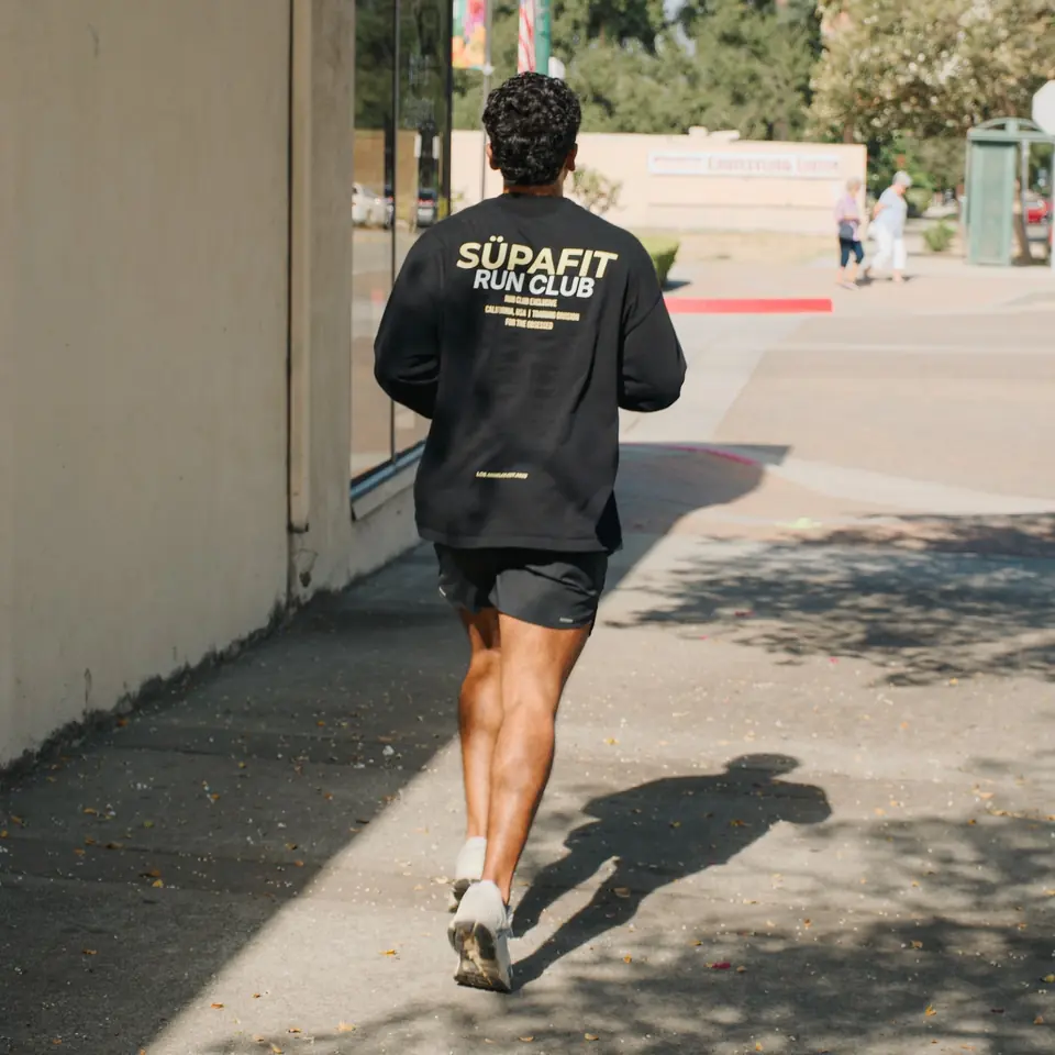 Runner in a SÜPAFIT Run Club long sleeve jogging down a sunny sidewalk