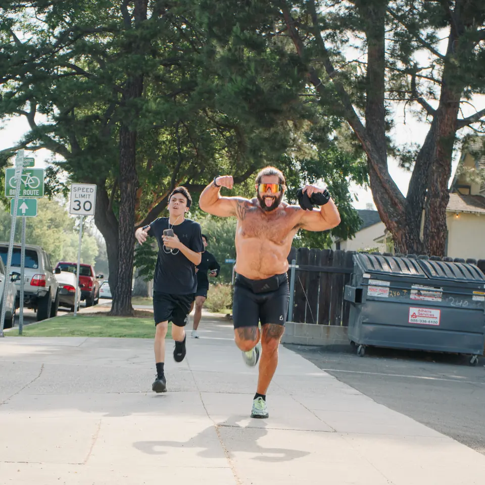 Runner with arms up mid stride next to a younger runner on a tree lined street