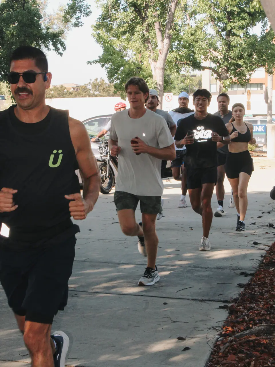 Runners in a tight pack jogging down a shaded Claremont sidewalk