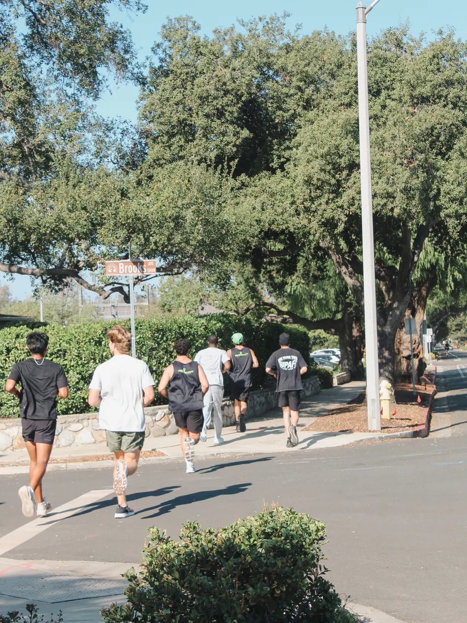 Small group running past a street sign under big oak trees in Claremont
