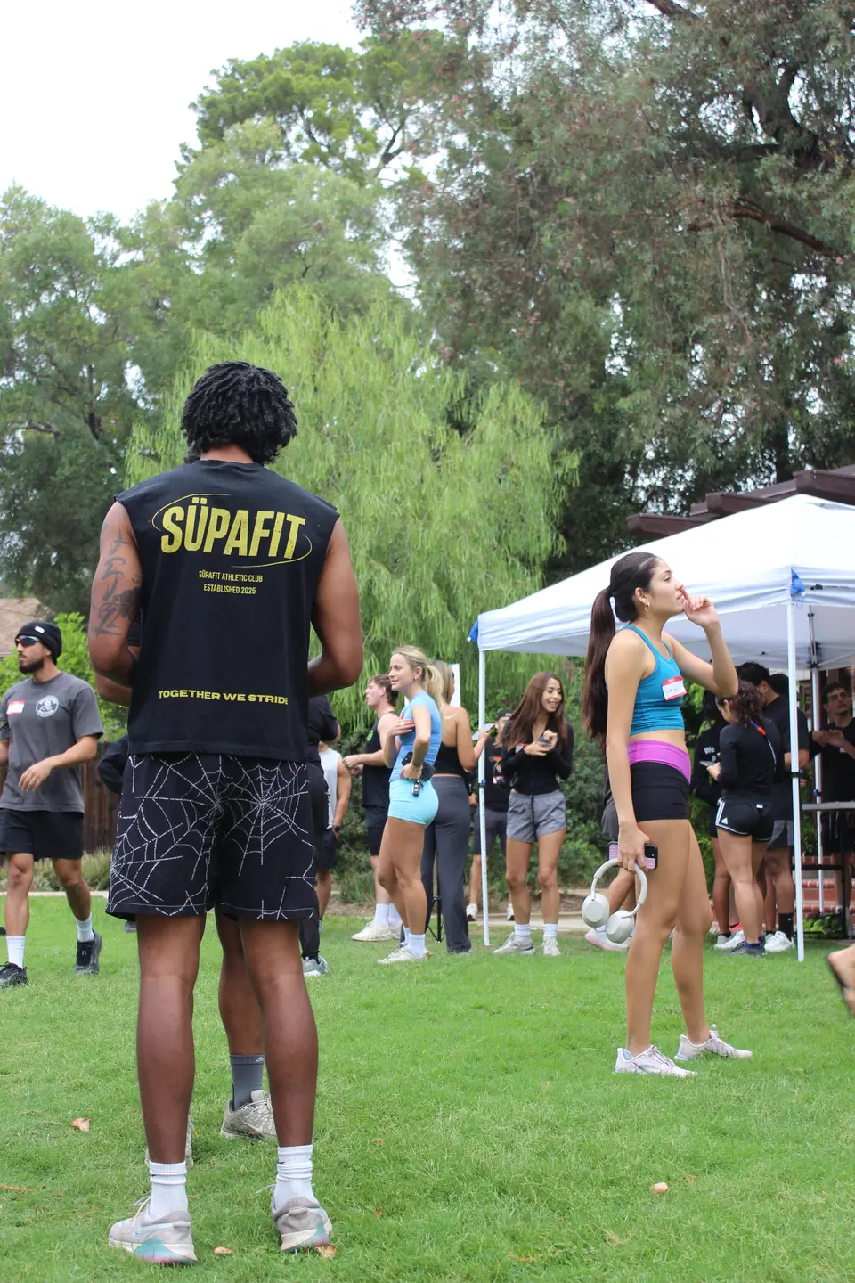 Runner in a SÜPAFIT Athletic Club tank standing on the grass as the crowd mingles