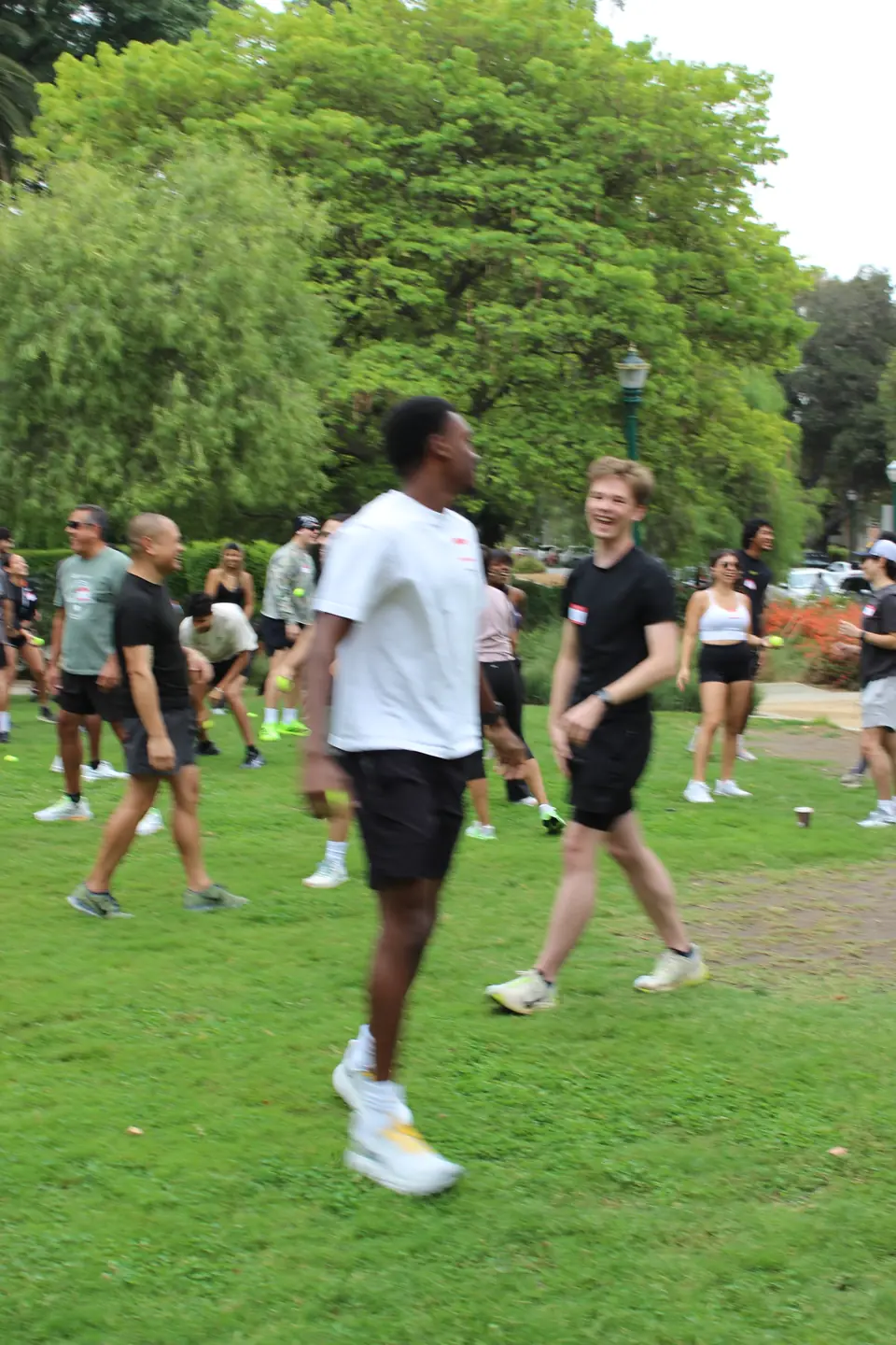 Two runners laughing during a warmup game with tennis balls on the grass